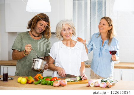Cheerful couple and old woman drinking wine and cooking in the kitchen at home 122655054