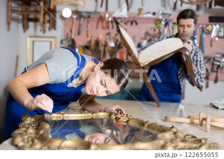 Girl restorer carefully covers carved wooden frame of antique wall mirror with thin layer of varnish Girl restorer carefully covers carved wooden frame of antique wall mirror with thin layer of varnish 122655055