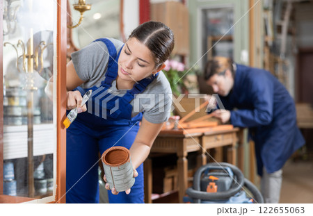 Professional furniture restorer renewing vintage chest of drawers in workshop 122655063