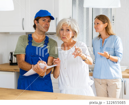 Mature housewife tells the plumber where to change the pipes in kitchen Mature housewife tells the plumber where to change the pipes in kitchen 122655085