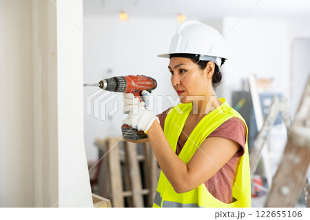 Asian woman repairer boring hole in wall with drill Asian woman repairer boring hole in wall with drill 122655106