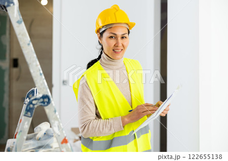 Woman foreman in a protective helmet and yellow vest checks the completed construction work on drawing Woman foreman in a protective helmet and yellow vest checks the completed construction work on drawing 122655138