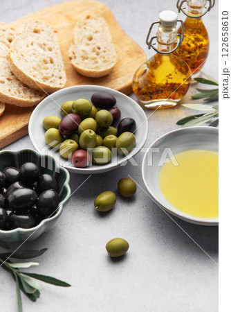 Bowls with green and black olives, olive oil and sliced bread on a wooden cutting board 122658610