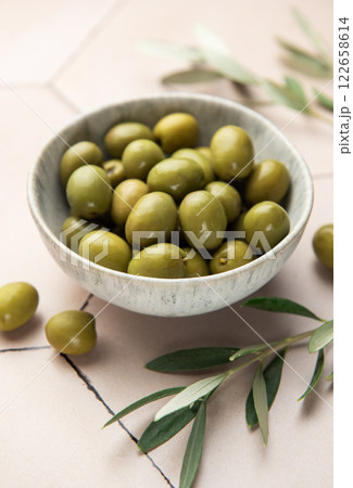 Green olives with olive branches resting in a bowl on a tiled surface Green olives with olive branches resting in a bowl on a tiled surface 122658614