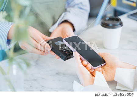 飲食店でテイクアウトコーヒーをスマートフォンのタッチ決済で購入する女性の手元 122659004