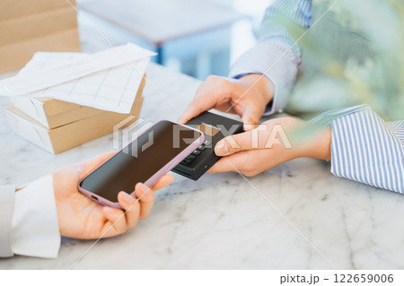 店舗で購入したテイクアウトの食事の支払いをスマートフォンのタッチで決済する女性の手元 店舗で購入したテイクアウトの食事の支払いをスマートフォンのタッチで決済する女性の手元 122659006