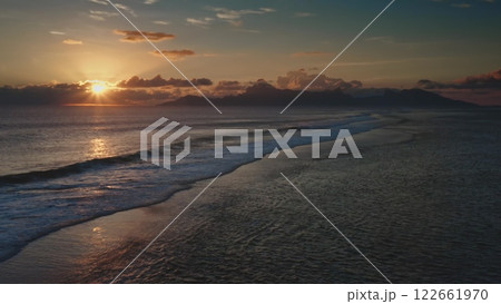 Golden sunset casting a magical glow over a tranquil ocean, with gentle waves lapping at the shore and majestic mountains rising in the background, evokes serenity Golden sunset casting a magical glow over a tranquil ocean, with gentle waves lapping at the shore and majestic mountains rising in the background, evokes serenity 122661970