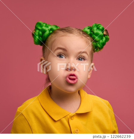 Portrait of playful child, preschool girl in yellow shirt and braided buns hairstyle emotionally making funny faces against pink studio background. Portrait of playful child, preschool girl in yellow shirt and braided buns hairstyle emotionally making funny faces against pink studio background. 122662239