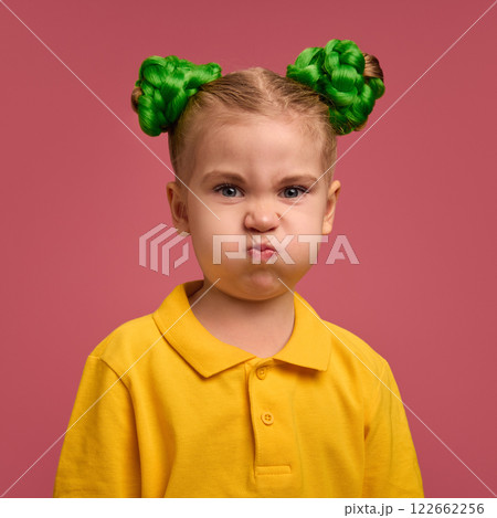 Portrait of preschool girl, child in yellow shirt making funny faces, grimacing against pink studio background. Portrait of preschool girl, child in yellow shirt making funny faces, grimacing against pink studio background. 122662256