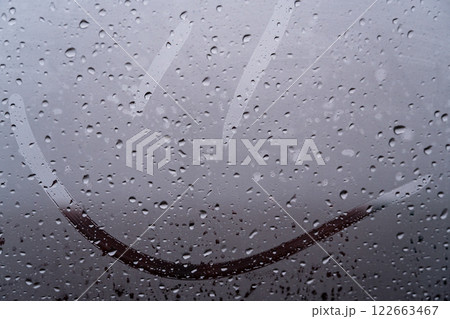 Cheerful smiley face etched on a foggy glass, surrounded by glistening raindrops. Nature's beauty brings moments of joy during rain 122663467