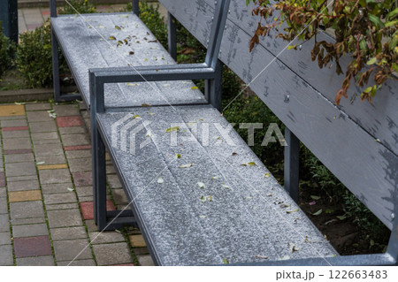 In a serene outdoor environment, a bench lies blanketed in fresh snow, surrounded by nature's muted winter colors and frost-covered greenery 122663483