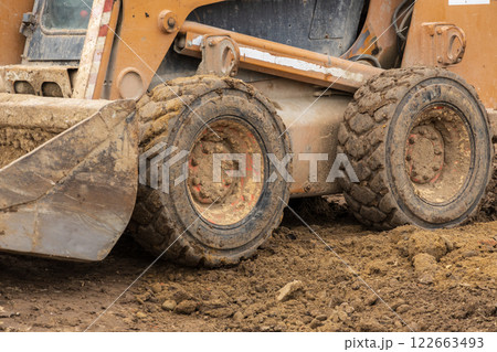 A backhoe and bulldozer are busy digging and maneuvering through dirt at an active construction site as workers coordinate their efforts nearby A backhoe and bulldozer are busy digging and maneuvering through dirt at an active construction site as workers coordinate their efforts nearby 122663493