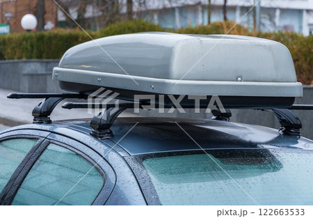 A sleek car is parked in an urban area amidst rain, showcasing its roof-mounted storage accessory, perfect for travel and adventure 122663533