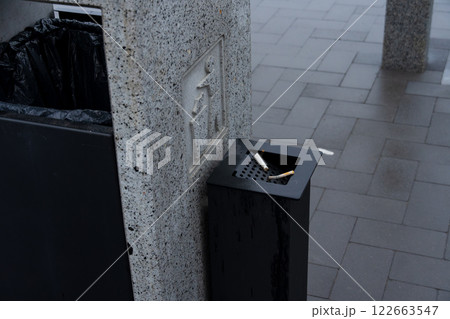 A dark trash bin stands beside a recycling container, emphasizing effective waste management and environmental conservation in the city 122663547