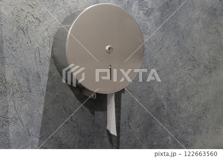 A round stainless steel toilet paper dispenser is installed in a gray wall, promoting hygiene and cleanliness in the restroom area A round stainless steel toilet paper dispenser is installed in a gray wall, promoting hygiene and cleanliness in the restroom area 122663560