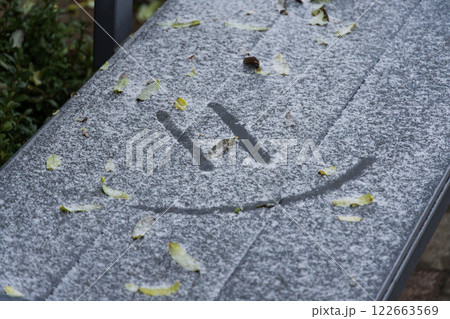 A bench in a winter landscape is blanketed with snow and frost, where a smiley face is playfully etched into the white layer A bench in a winter landscape is blanketed with snow and frost, where a smiley face is playfully etched into the white layer 122663569