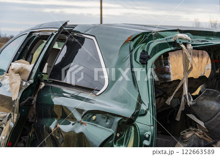 A wrecked car with severe damage to its roof and side is observed in a rural environment, highlighting the dangers of road incidents 122663589