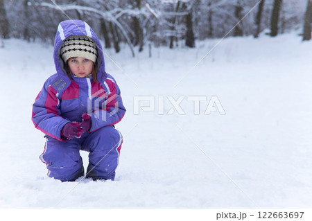 Cute serious thinker child girl in overalls walks in a winter forest park 122663697