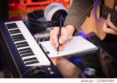 male songwriter hand writing a hit song by acoustic guitar and music keyboard in home studio. song writing concept 122663984