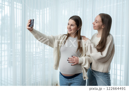 Young pregnant woman taking a selfie with her female friend at home, smiling and enjoying the moment, with copy space. friendship, maternity, capturing special memories during pregnancy. Young pregnant woman taking a selfie with her female friend at home, smiling and enjoying the moment, with copy space. friendship, maternity, capturing special memories during pregnancy. 122664491