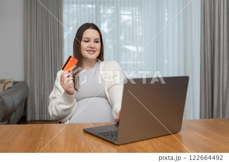 Relaxed pregnant woman shopping online with a credit card and laptop at home with copy space for text. Concept of convenience, ecommerce, motherhood and embracing technology in everyday life. Relaxed pregnant woman shopping online with a credit card and laptop at home with copy space for text. Concept of convenience, ecommerce, motherhood and embracing technology in everyday life. 122664492