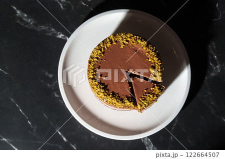 Top view Dubai chocolate cheesecake with pistachio paste and kataifi covered in chocolate ganache on white plate. Black marble background with copy space. Indulgence, gourmet desserts, art of culinary Top view Dubai chocolate cheesecake with pistachio paste and kataifi covered in chocolate ganache on white plate. Black marble background with copy space. Indulgence, gourmet desserts, art of culinary 122664507