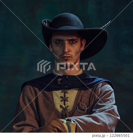 Portrait of brave man, medieval pirate in feathered hat staring intensely, against dark green vintage background. Portrait of brave man, medieval pirate in feathered hat staring intensely, against dark green vintage background. 122665501