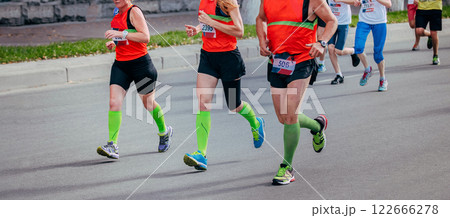 two women and man running marathon in city, green compression socks on his feet 122666278