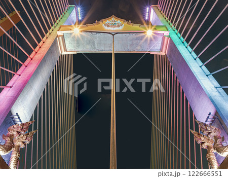 The girders of a cable-stayed bridge at Thotsamarachan Bridge or King Rama X Bridge with Two golden yellow Naga sculptures on concrete pillars at Night. 122666551