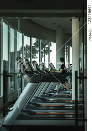 A young woman with long hair and wearing a black sports outfit is working out on modern electric treadmills. A young woman with long hair and wearing a black sports outfit is working out on modern electric treadmills. 122666694
