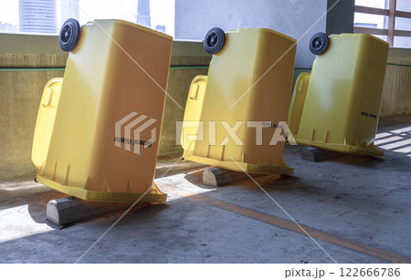 Perspective view of Yellow large plastic rubbish bins and turn upside down to dry near concrete wall on parking lot of condominium building. 122666786