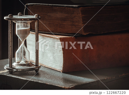 View of Silver hourglass (Sandglass) with Ancient books on dark background. View of Silver hourglass (Sandglass) with Ancient books on dark background. 122667220