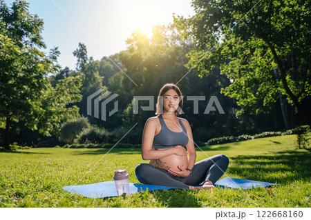 Dark-haired caucasian pregnant woman sitting on the lawn and feeling peaceful and calm 122668160