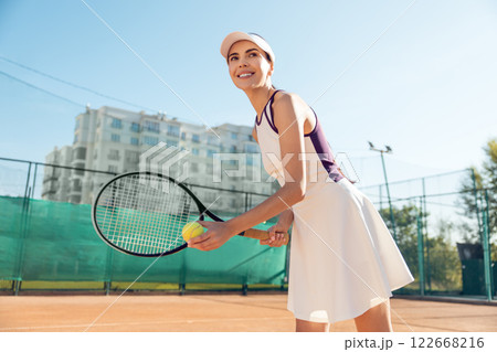 Slim woman playing tennis on court holding racket in motion enjoying outdoor summer workout Slim woman playing tennis on court holding racket in motion enjoying outdoor summer workout 122668216
