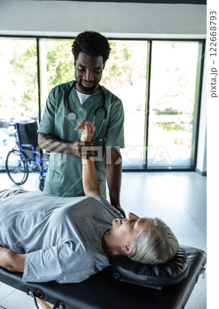 Male dark-skinned doctor working on arms stretching of his female patient Male dark-skinned doctor working on arms stretching of his female patient 122668793