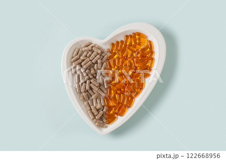 Medicinal herb, plant based supplements and omega oil pills in shape of heart on blue background. View from above. Healthcare concept. Medicinal herb, plant based supplements and omega oil pills in shape of heart on blue background. View from above. Healthcare concept. 122668956