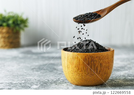 black sesame seeds falling from spoon in bowl on table 122669558