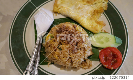 Fried rice with crispy shallots and a fried egg, slice of cucumber and tomato, a delicious blend of flavors and textures. Fried rice with crispy shallots and a fried egg, slice of cucumber and tomato, a delicious blend of flavors and textures. 122670314