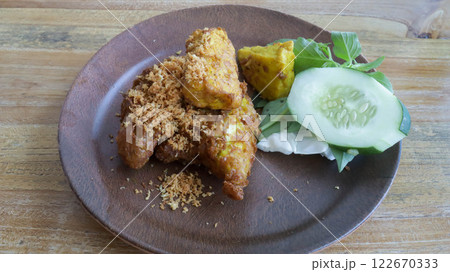 Savor Ayam Penyet, East Javanese fried chicken, pounded for tenderness, served with sambal, slice of cucumber, fried tofu, and tempeh. Savor Ayam Penyet, East Javanese fried chicken, pounded for tenderness, served with sambal, slice of cucumber, fried tofu, and tempeh. 122670333