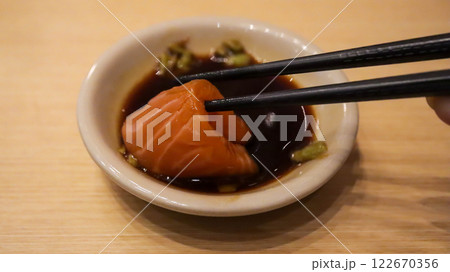 Hand is dipping salmon sushi into Shoyu sauce using chopsticks. 122670356