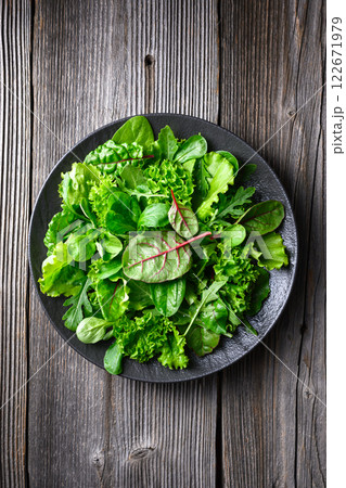 Mix of fresh juicy raw salad greens in black plate on wooden table 122671979