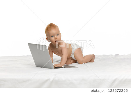 Adorable baby, girl in diaper sitting in bed with laptop against white studio background. Early development, education, cartoons Adorable baby, girl in diaper sitting in bed with laptop against white studio background. Early development, education, cartoons 122672296