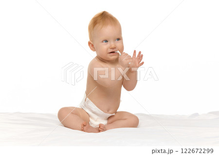 Cute, smiling baby, girl in diaper sitting in bed with toothbrush against white studio background Cute, smiling baby, girl in diaper sitting in bed with toothbrush against white studio background 122672299