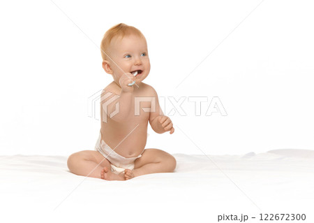 Adorable, smiling baby, girl in diaper sitting in bed with toothbrush against white studio background 122672300