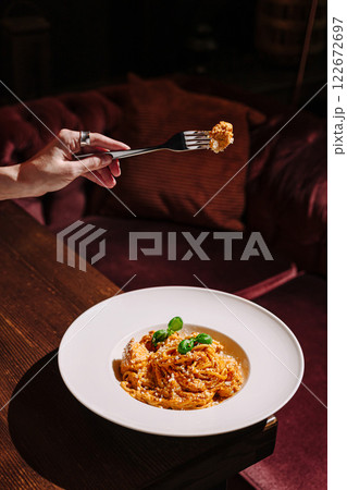 Beautifully plated pasta dish being enjoyed in a cozy dining setting with warm lighting 122672697