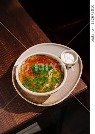 Delicious traditional soup with fresh herbs served on a wooden table in a cozy setting 122672810