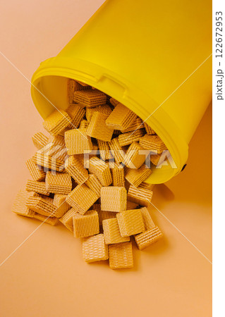 Yellow container tipped over, spilling crunchy wafer squares across a pastel background 122672953