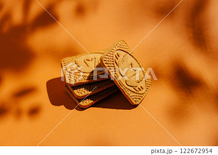 Delightful cookies stacked on a warm orange background with intricate designs and soft shadow play 122672954