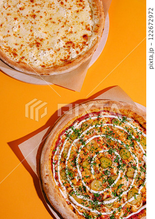 Delicious pizzas displayed on a vibrant orange background, showcasing cheese and unique toppings with fresh ingredients 122672972