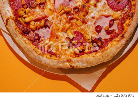 Delicious pepperoni and ham pizza topped with diced pineapples on a vibrant orange background Delicious pepperoni and ham pizza topped with diced pineapples on a vibrant orange background 122672973